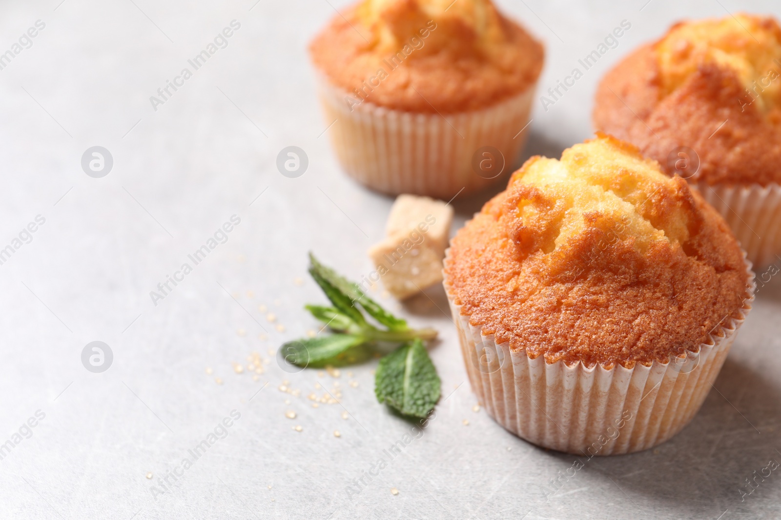 Photo of Delicious sweet muffins and brown sugar on light grey textured table, closeup. Space for text