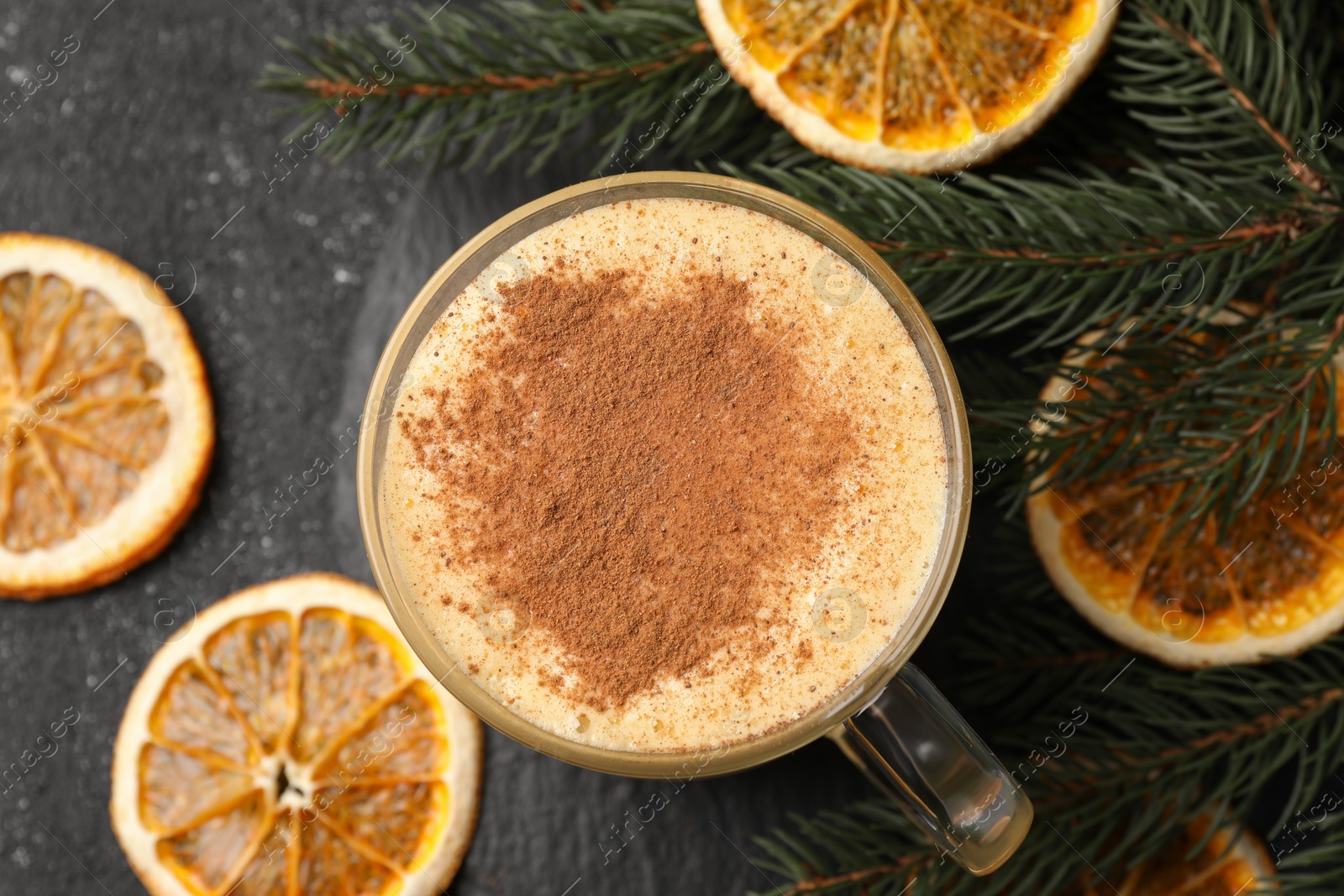 Photo of Glass cup of delicious eggnog with cinnamon and dried orange slices on gray table, flat lay