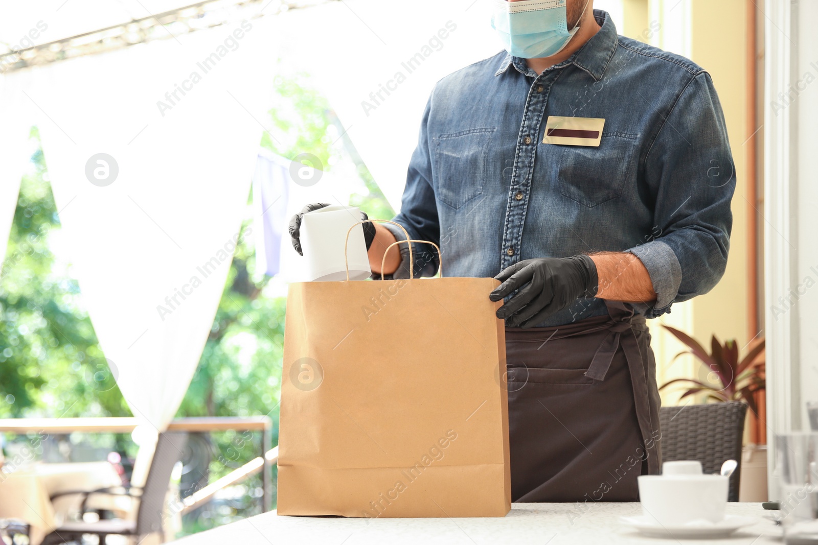 Photo of Waiter packing takeout order in restaurant, closeup. Food service during coronavirus quarantine