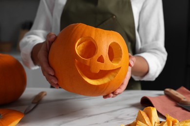 Photo of Woman holding carved pumpkin for Halloween at white marble table, closeup