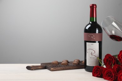 Photo of Bottle of red wine, beautiful roses and chocolate candies on white wooden table. Space for text