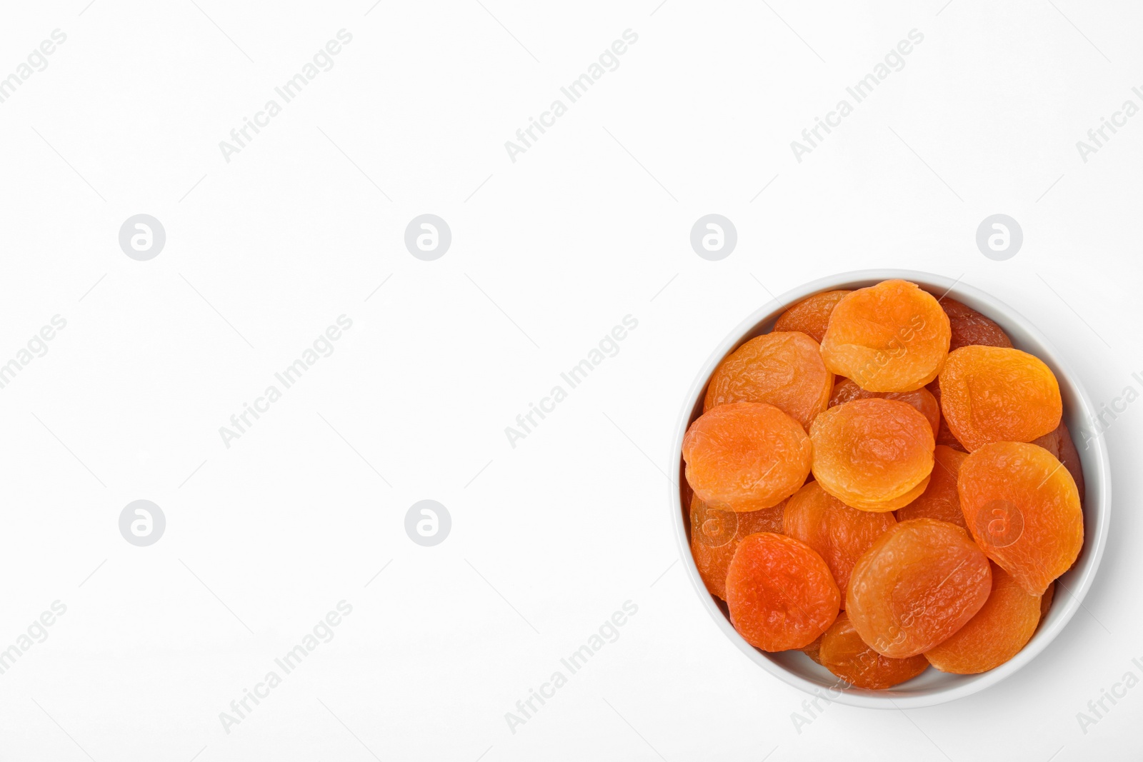 Photo of Bowl of dried apricots on white background, top view with space for text. Healthy fruit