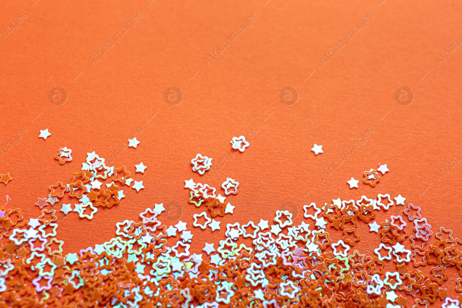 Photo of Shiny bright star shaped glitter on orange background. Space for text