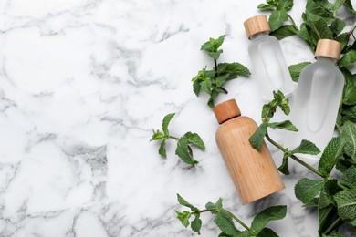 Photo of Bottles of mint essential oil and fresh leaves on white marble table, flat lay. Space for text