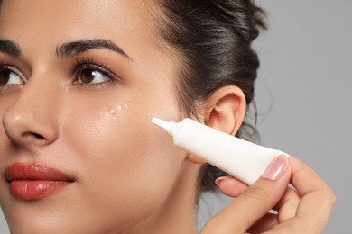 Photo of Woman applying cream under eyes on grey background, closeup. Skin care