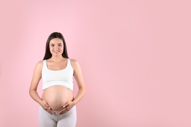 Beautiful pregnant woman holding hands on belly against color background. Space for text