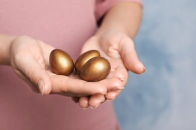 Photo of Woman holding golden eggs on light blue background, closeup