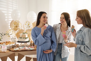 Photo of Happy pregnant woman and her friends with tasty cookies at baby shower party