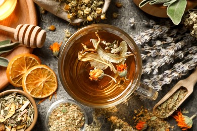 Photo of Freshly brewed tea and dried herbs on grey table, flat lay