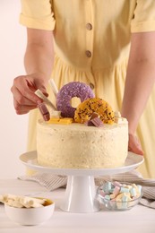 Woman decorating delicious cake with sweets at white wooden table, closeup