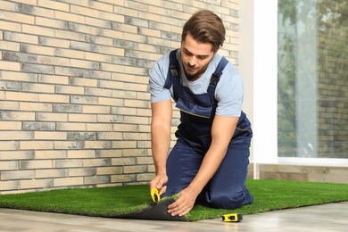 Man in uniform cutting artificial grass carpet indoors