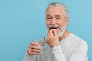 Photo of Senior man with glass of water taking pill on light blue background