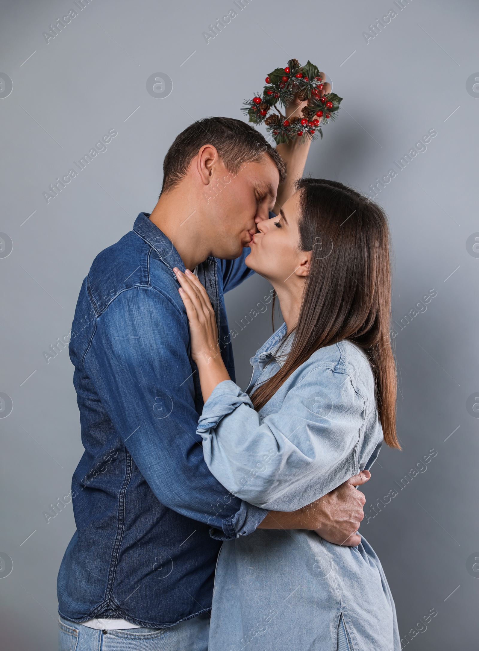 Photo of Happy couple kissing under mistletoe wreath on grey background