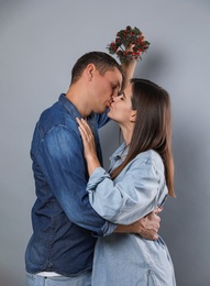 Happy couple kissing under mistletoe wreath on grey background