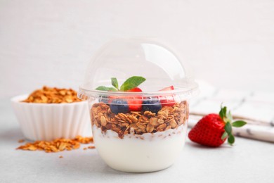 Photo of Tasty granola with berries and yogurt in plastic cup on light table