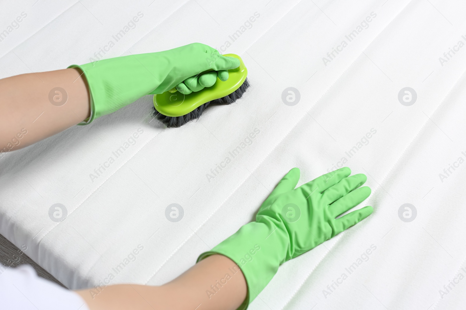 Photo of Woman in green gloves cleaning white mattress with brush, closeup