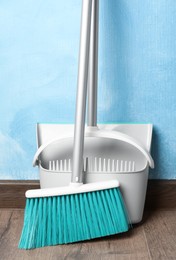 Photo of Plastic broom with dustpan near light blue wall indoors