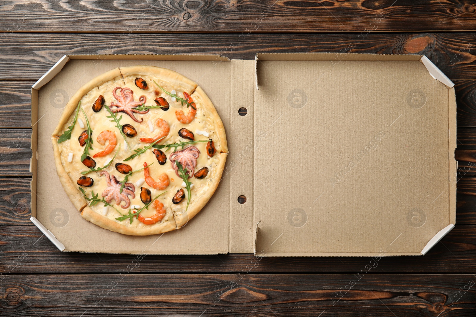 Photo of Delicious seafood pizza in cardboard box on wooden table, top view