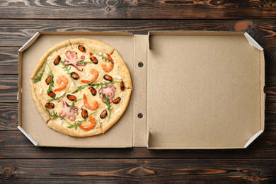 Delicious seafood pizza in cardboard box on wooden table, top view