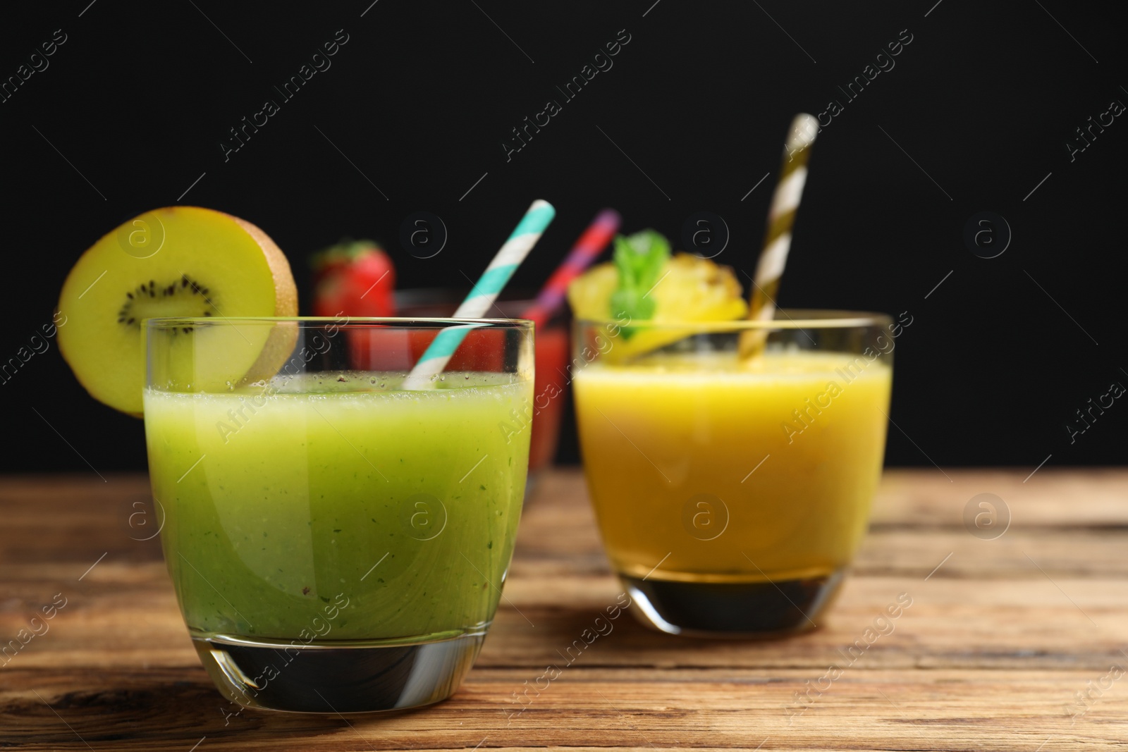 Photo of Delicious colorful juices in glasses on wooden table, closeup