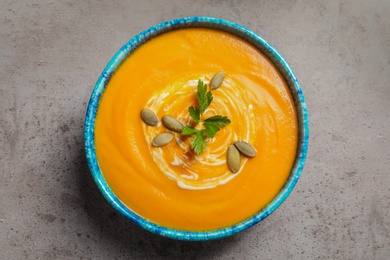 Photo of Bowl with tasty pumpkin soup on gray table, top view