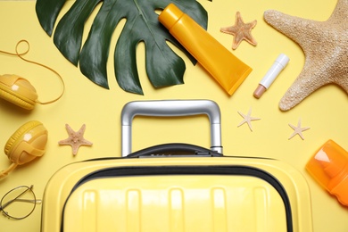 Photo of Flat lay composition with suitcase and sun protection products on yellow background