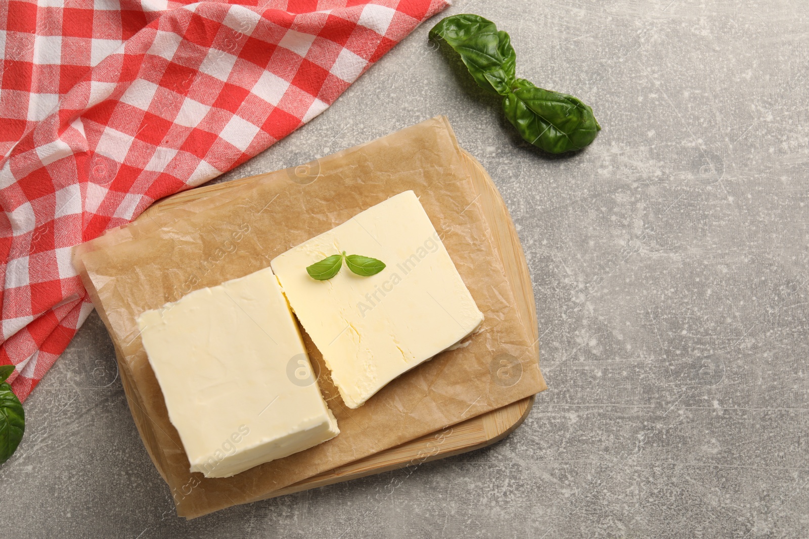 Photo of Block of tasty butter with basil on grey table, top view. Space for text