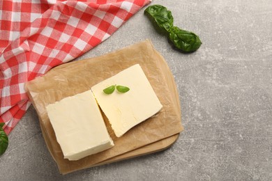 Block of tasty butter with basil on grey table, top view. Space for text