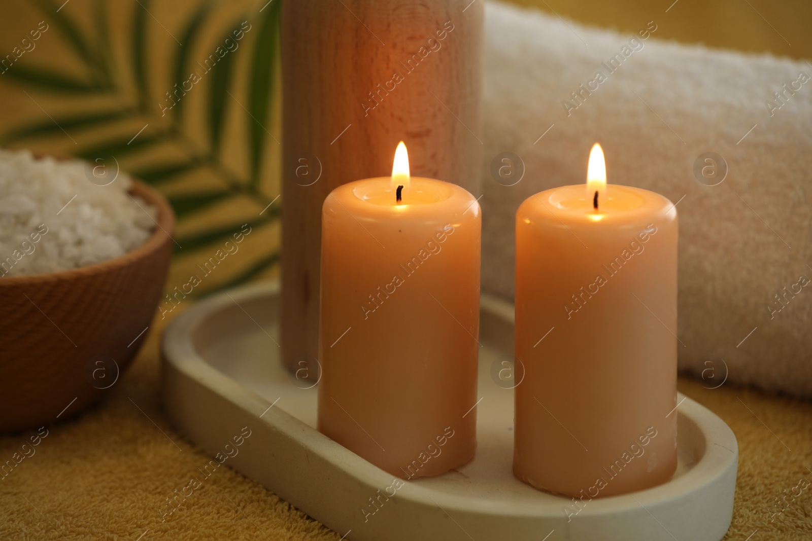 Photo of Spa composition with burning candles and sea salt on soft yellow fabric
