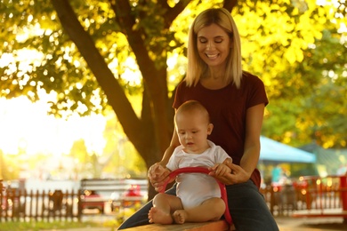 Photo of Nanny and cute baby sitting on seesaw outdoors
