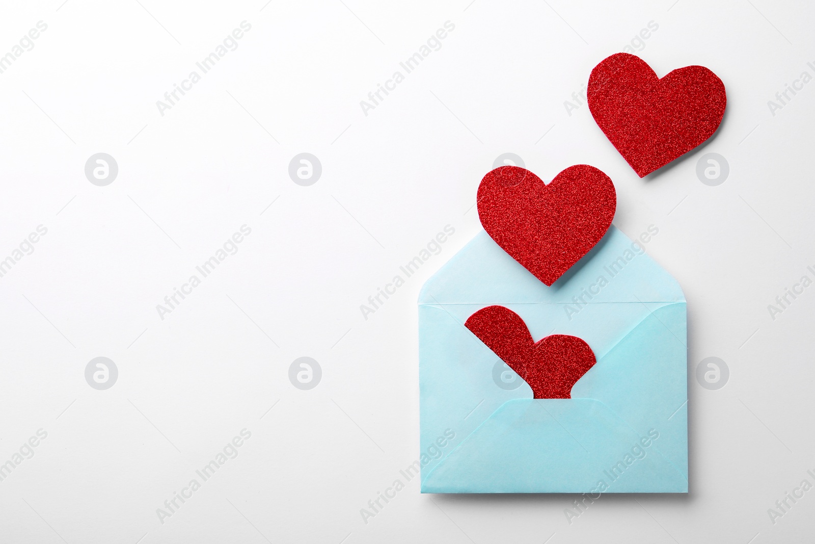 Photo of Red shiny paper hearts and envelope on white background, top view