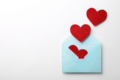 Photo of Red shiny paper hearts and envelope on white background, top view