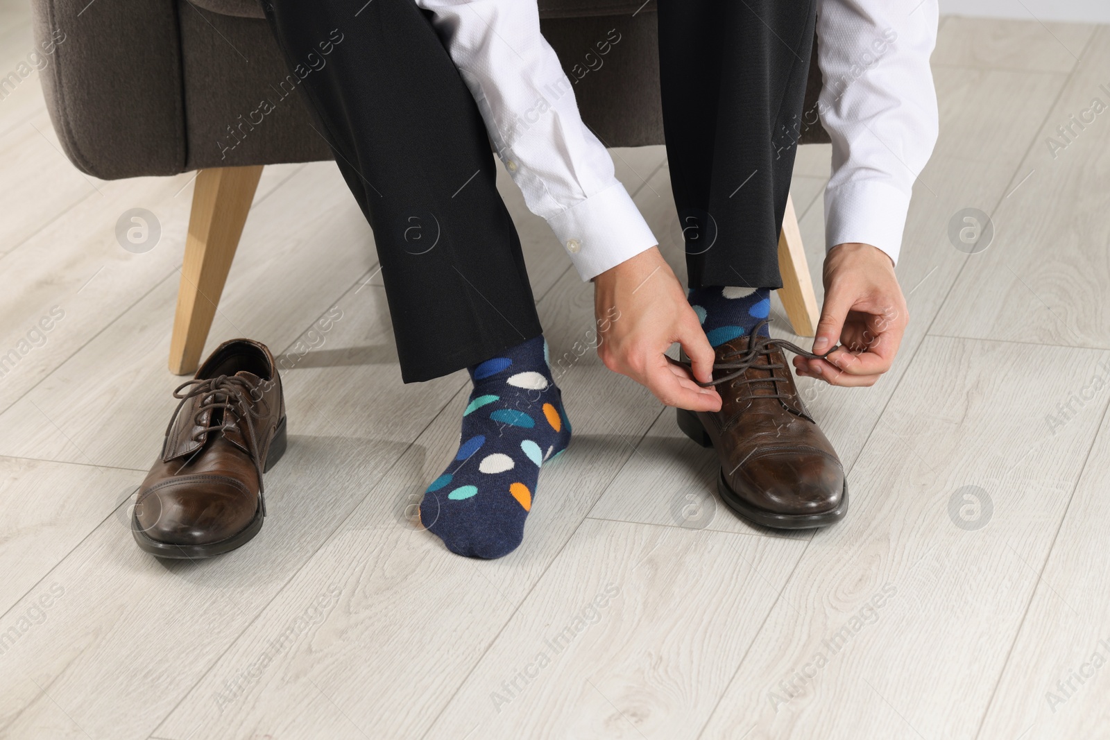 Photo of Man with colorful socks putting on stylish shoes indoors, closeup