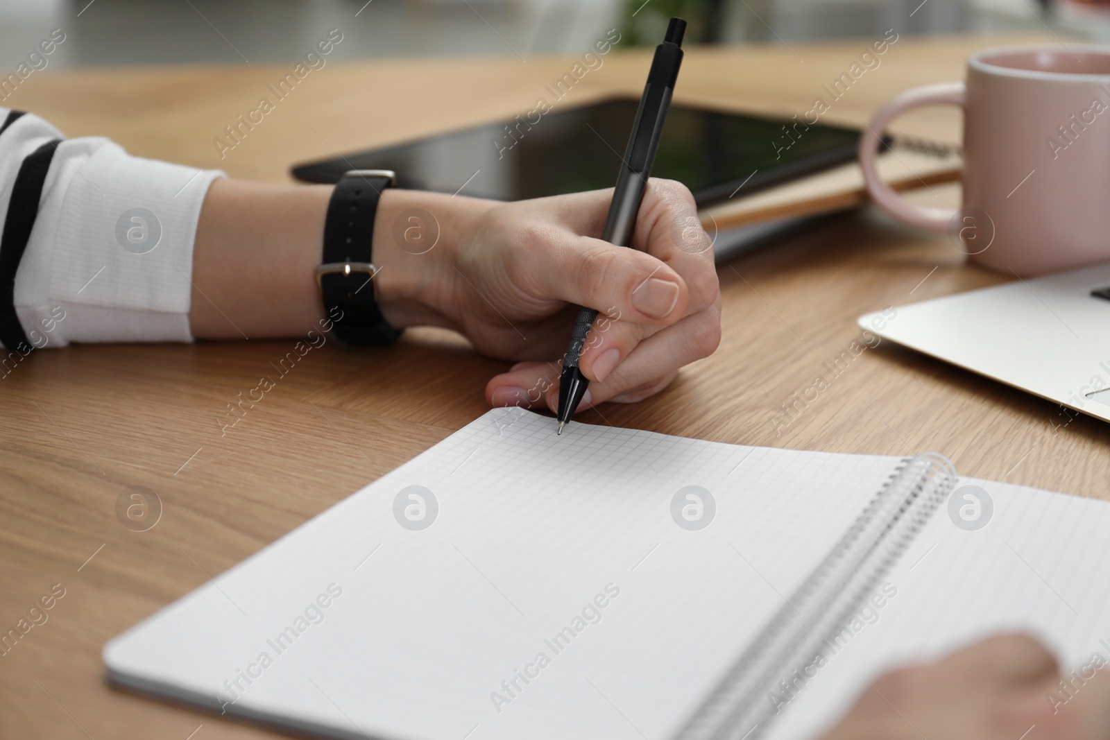 Photo of Left-handed woman writing in notebook at wooden table, closeup