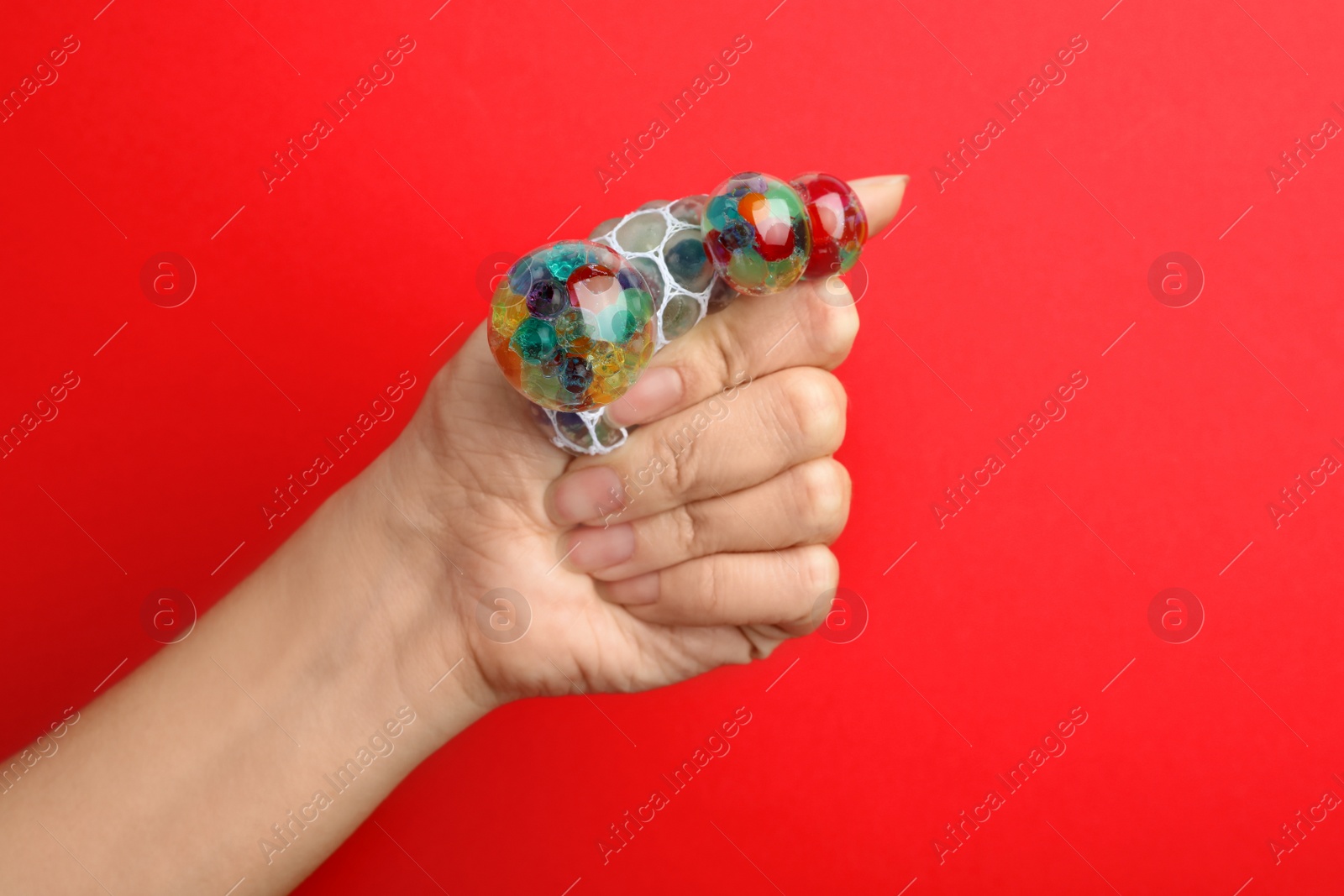 Photo of Woman squeezing colorful slime on red background, closeup. Antistress toy