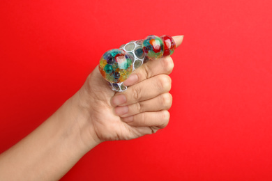 Woman squeezing colorful slime on red background, closeup. Antistress toy