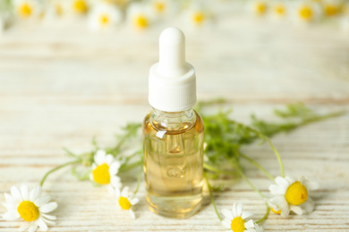 Bottle of essential oil and chamomiles on white wooden table