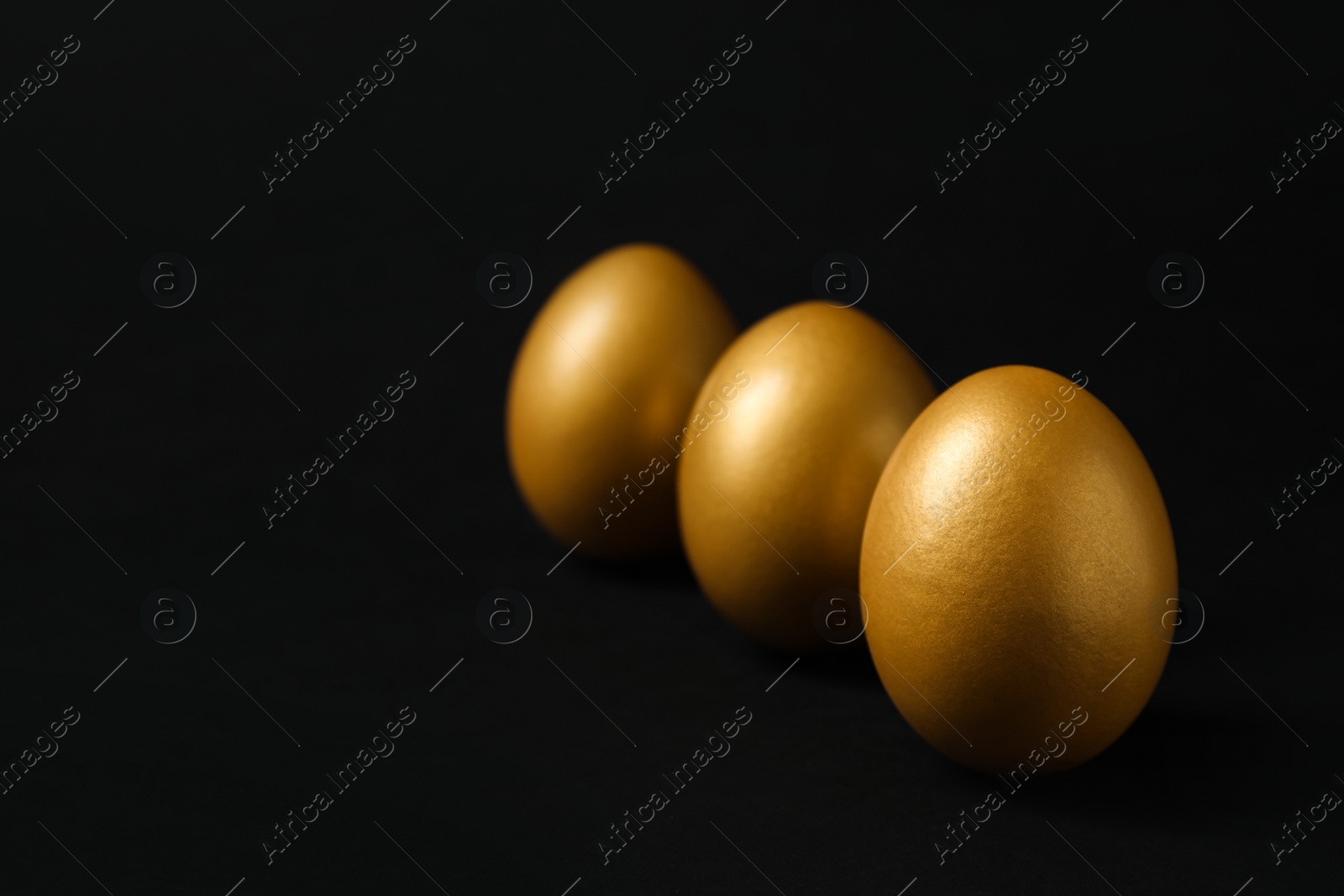 Photo of Shiny golden eggs on black background, space for text