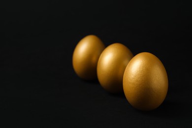 Photo of Shiny golden eggs on black background, space for text