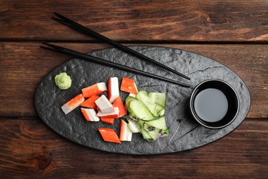 Photo of Fresh crab sticks with cucumber and soy sauce served on wooden table, flat lay