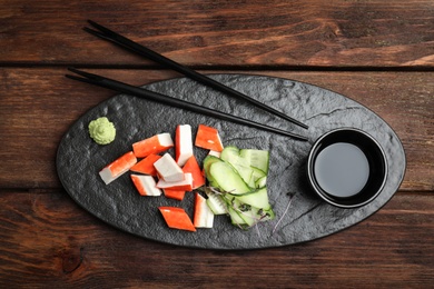 Fresh crab sticks with cucumber and soy sauce served on wooden table, flat lay