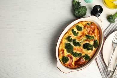 Tasty broccoli casserole in baking dish on white wooden table, flat lay. Space for text