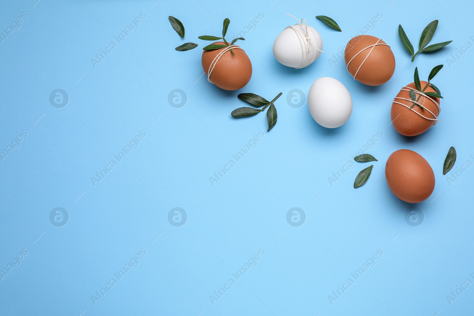 Photo of Beautifully decorated Easter eggs and green leaves on light blue background, flat lay. Space for text