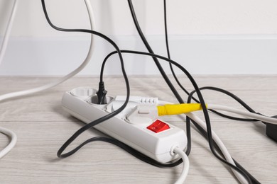 Photo of Power strip with electrical plugs on white floor indoors, closeup