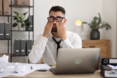 Overwhelmed man sitting at table with laptop and documents in office