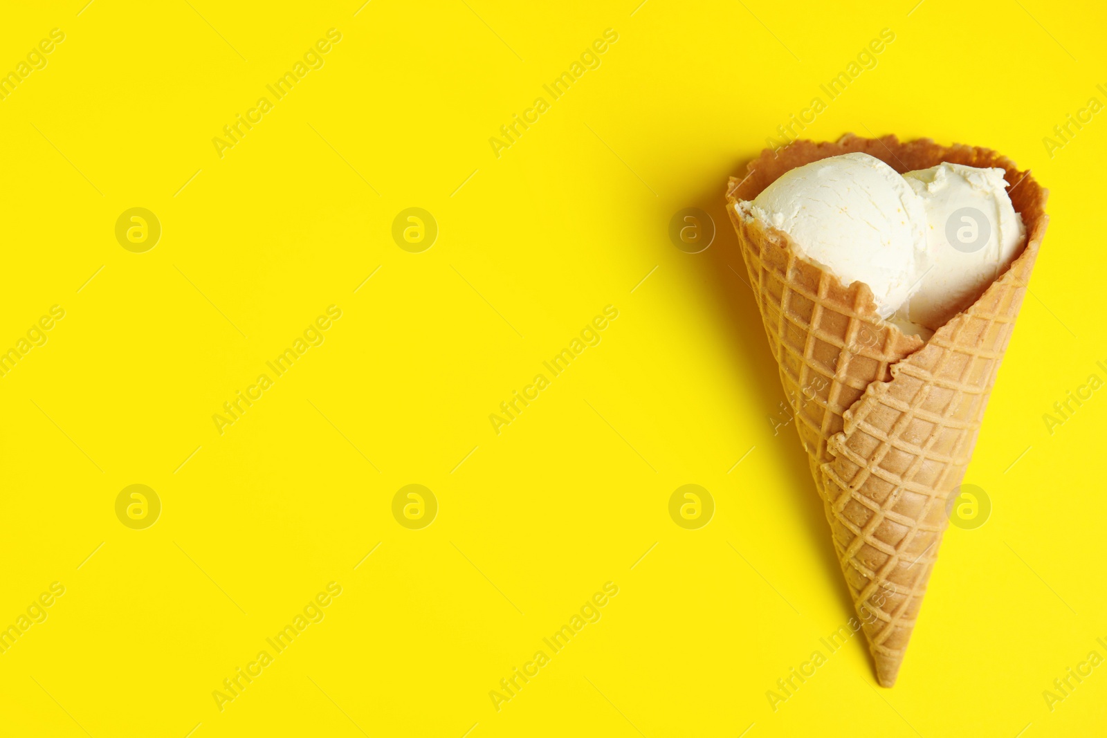 Photo of Delicious vanilla ice cream in wafer cone on yellow background, top view. Space for text