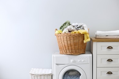 Photo of Wicker basket with dirty laundry on washing machine indoors, space for text