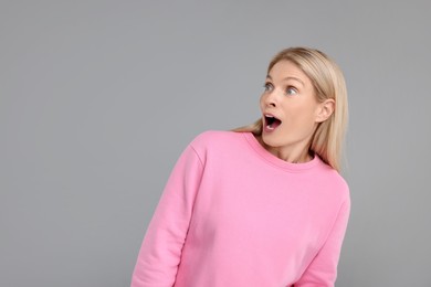 Portrait of surprised woman on grey background, space for text