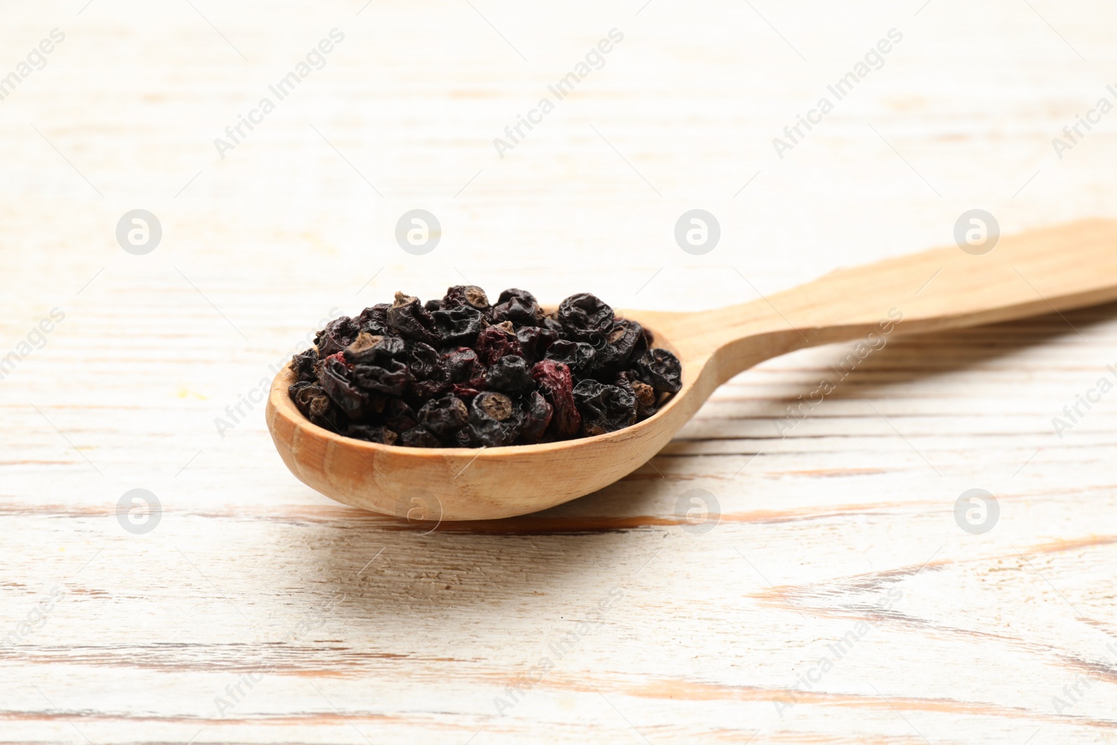 Photo of Wooden spoon with dried black currant berries on white table, closeup