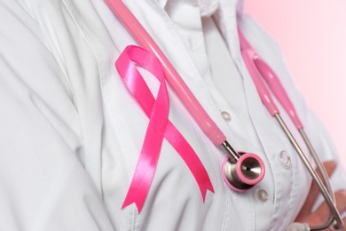 Female doctor with pink ribbon and stethoscope on color background, closeup. Breast cancer concept